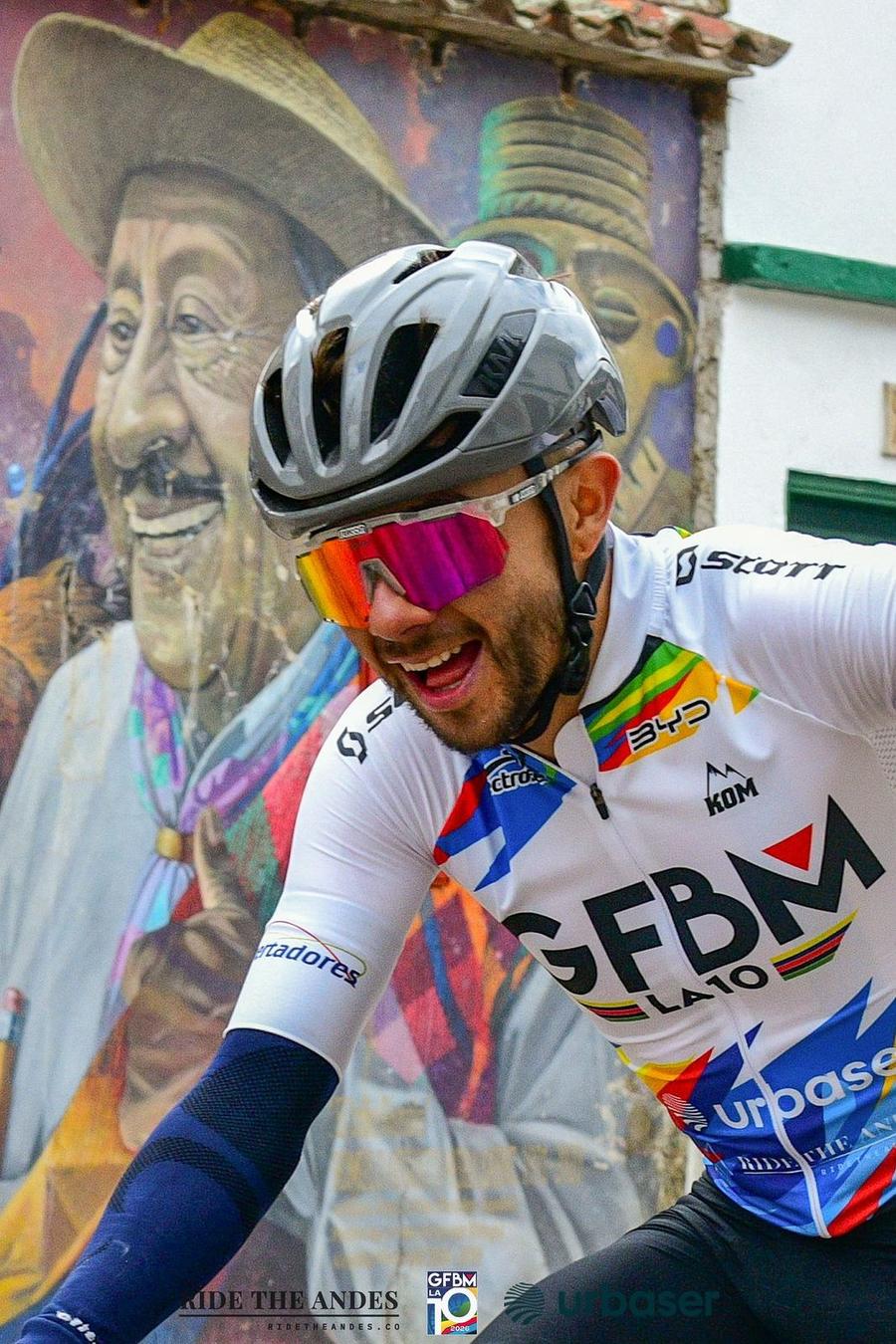 A laughing rider passes a large mural of a Boyacá farmer in Monguí during the Gran Fondo
