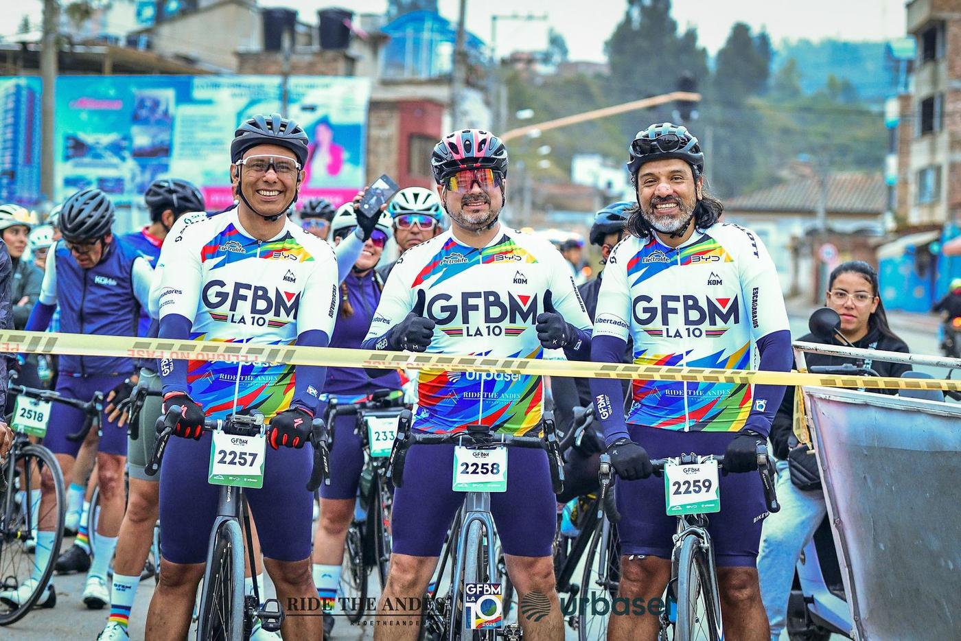 Three riders smile behind the start tape of the 2026 Gran Fondo Boyacá Mundial in Duitama, Ride The Andes on the front of their official jerseys